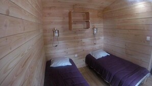 A cabin with two beds, wooden walls, a shelf, and a light fixture.