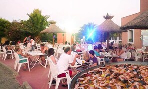 An outdoor dining area with tables and chairs, a large seafood display, and thatched umbrellas. - ZEcamping 3 étoiles piscine chauffée animaux acceptés roulotte 15m2 (Portel-des-Corbières)