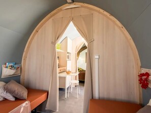 Ein gemütlicher Raum mit gewölbter Holzbalkendecke, einem kleinen Schreibtisch, einem Stuhl und einem Bett mit orangefarbener Bettwäsche.
