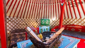 A traditional yurt interior with a woven basket on a table, a sleeping area with a patterned rug, and a small green stool. - ZEcamping 1 étoile pet friendly mobil-home BBQ 28m2 5 pers (Plessix-Balisson)