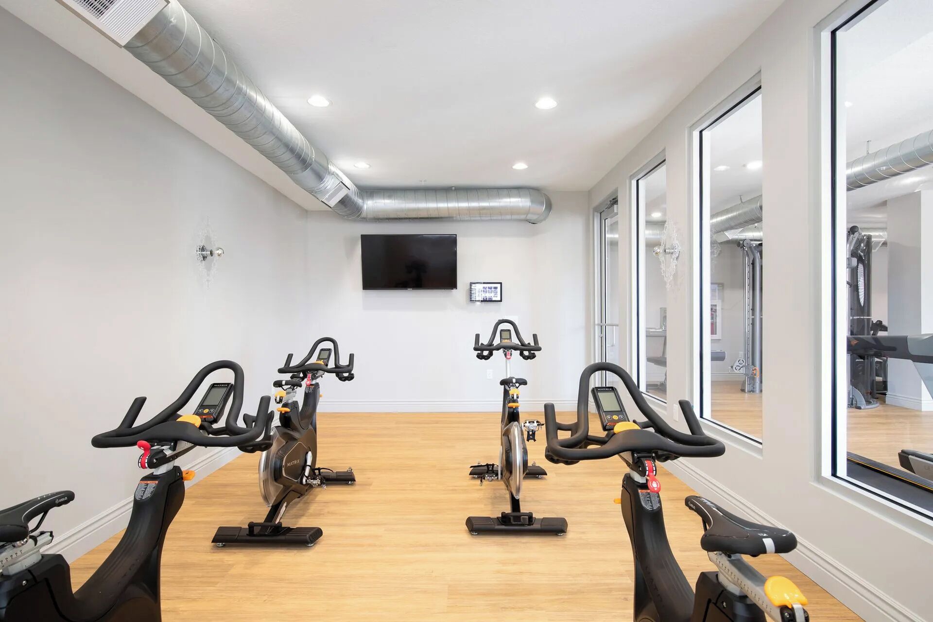 A gym with stationary bikes, a TV, and large windows.