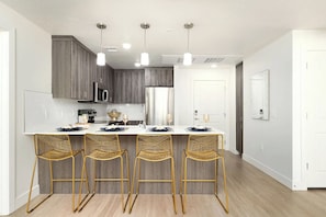 Una cocina moderna con una isla central, taburetes de bar, electrodomésticos de acero inoxidable e iluminación colgante.