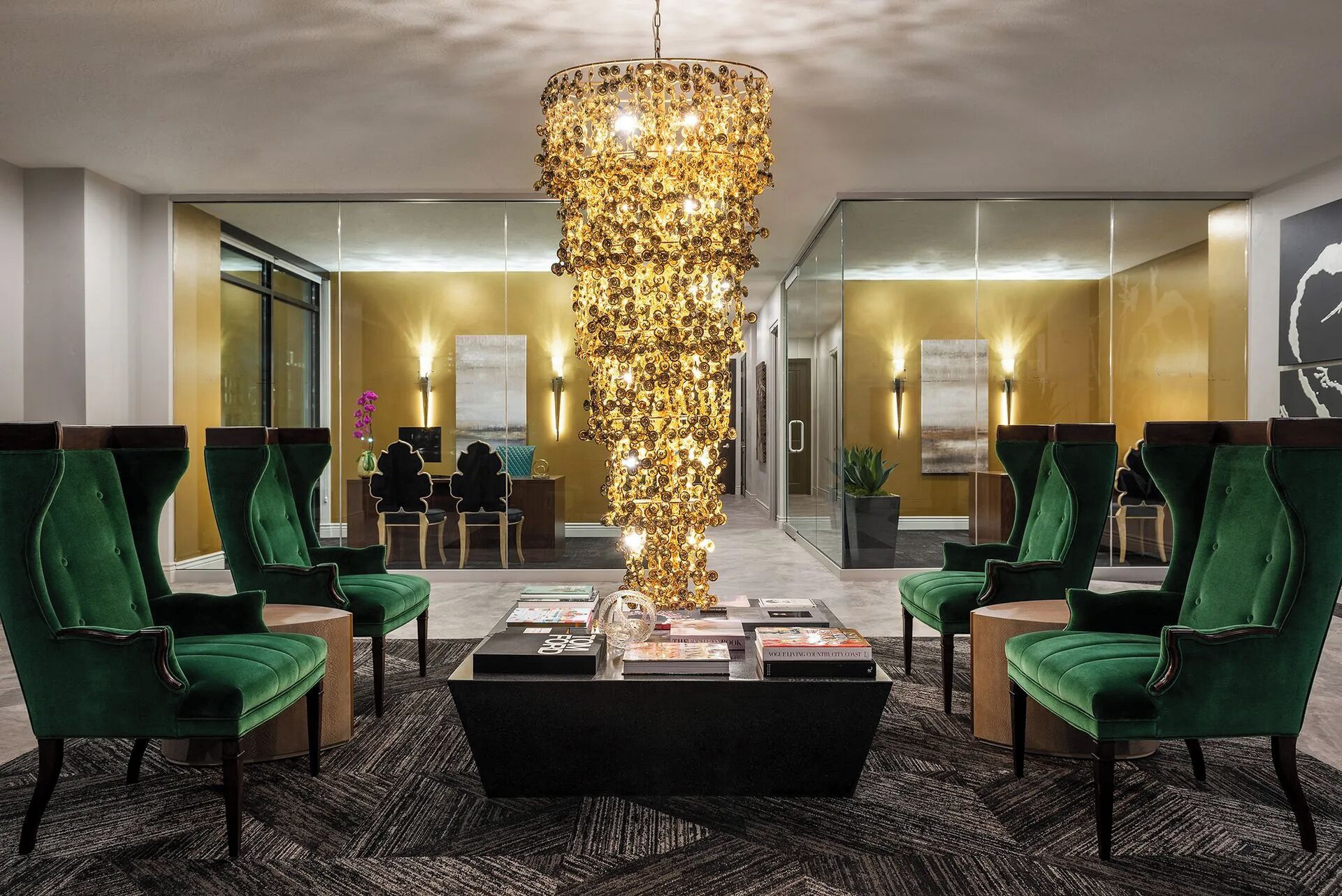 Eine Lobby mit grünen Polstersesseln, einem schwarzen Couchtisch in der Mitte und einer dekorativen Leuchte.