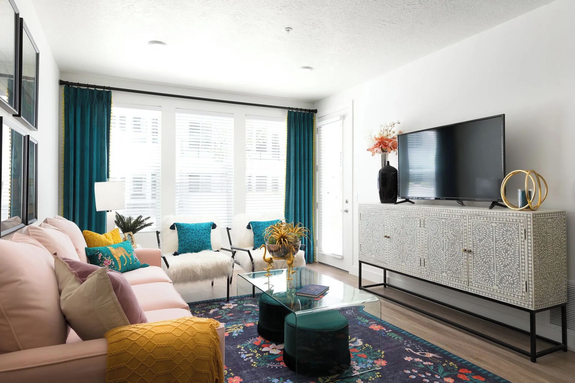 A modern living room with a sofa, a glass coffee table, a TV on a cabinet, and a view of the outside through large windows.
