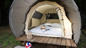 Une tente en forme de dôme, avec un lit à l’intérieur, une table de pique-nique et un filet de volley-ball.