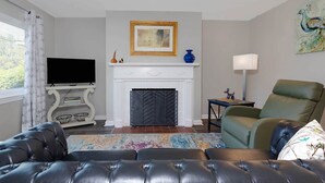 A living room with a fireplace, a television, a green armchair, and a colorful rug. - Premium 2BR Retreat by St. Francis (Columbus)