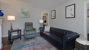 A living room with a black leather sofa, a green armchair, a patterned rug, and framed artwork on the walls. - Premium 2BR Retreat by St. Francis (Columbus)