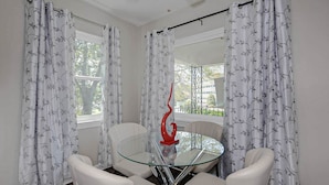 A room with a glass table and white chairs, two windows with curtains, and a red sculpture. - Premium 2BR Retreat by St. Francis (Columbus)