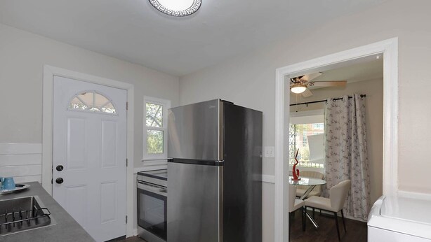A compact kitchen with a stainless steel refrigerator, a built-in oven, and a small dining area with a table and chairs. - Premium 2BR Retreat by St. Francis (Columbus)