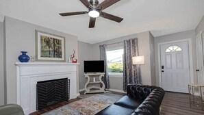 A living room with a fireplace, a television, a sofa, and a ceiling fan. - Modern 2BR Steps to St Francis (Columbus)