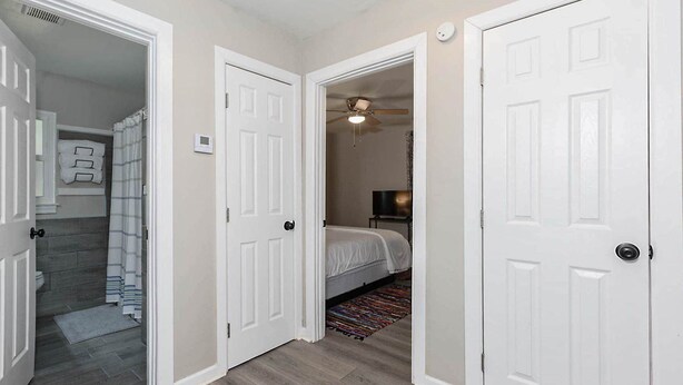 A hallway with two white doors, a bathroom with a shower, and a bedroom with a bed and a TV. - Modern 2BR Steps to St Francis (Columbus)