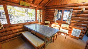 Ein Holzblockhaus-Interieur mit einem Holztisch, Bänken und einem Schild mit der Aufschrift 'OUR CABIN'.