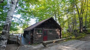 Eine Blockhütte mit roter Tür, einer Veranda und einem kleinen Fenster.