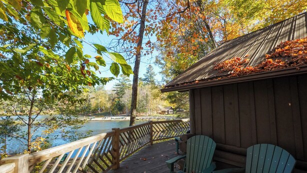 Eine Holzterrasse mit Stühlen, die auf einen See blickt, ein Blockhaus und ein Holzgeländer.
