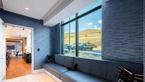 Un vestíbulo de hotel moderno con zona de estar, mostrador de recepción y vista a coches aparcados y colinas.