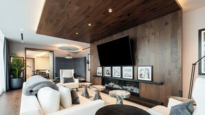 Una sala de estar moderna con un televisor de pantalla plana grande montado en la pared, una chimenea y un área de descanso con sofá y mesa de centro.