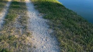 Un fiume tranquillo con un sentiero sterrato, case e un camino alto sullo sfondo.