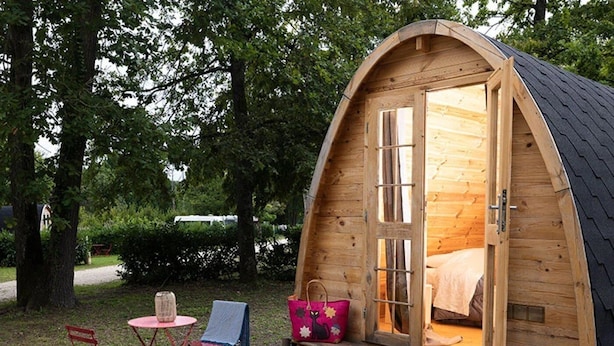 Eine Holzhütte mit einem Bett im Inneren, einem Picknicktisch und zwei Stühlen davor.