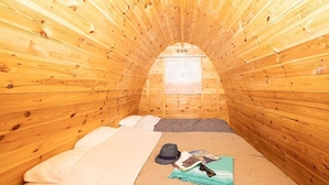 Ein gemütliches Schlafzimmer im Dachgeschoss mit Holzwänden, einem Bett, einem Fenster und einem kleinen Tisch mit persönlichen Gegenständen.