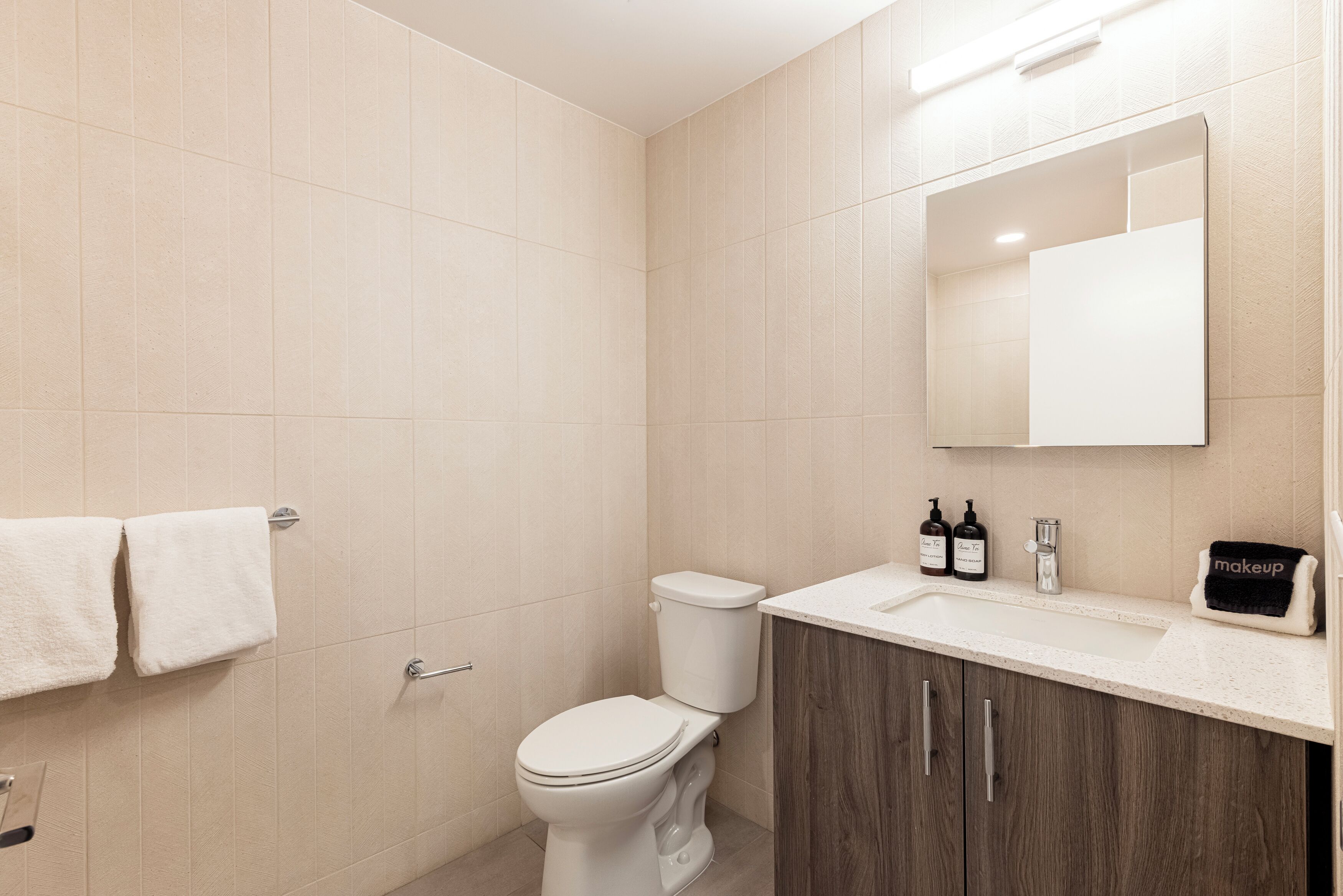 A bathroom with a toilet, sink, mirror, and two towels.