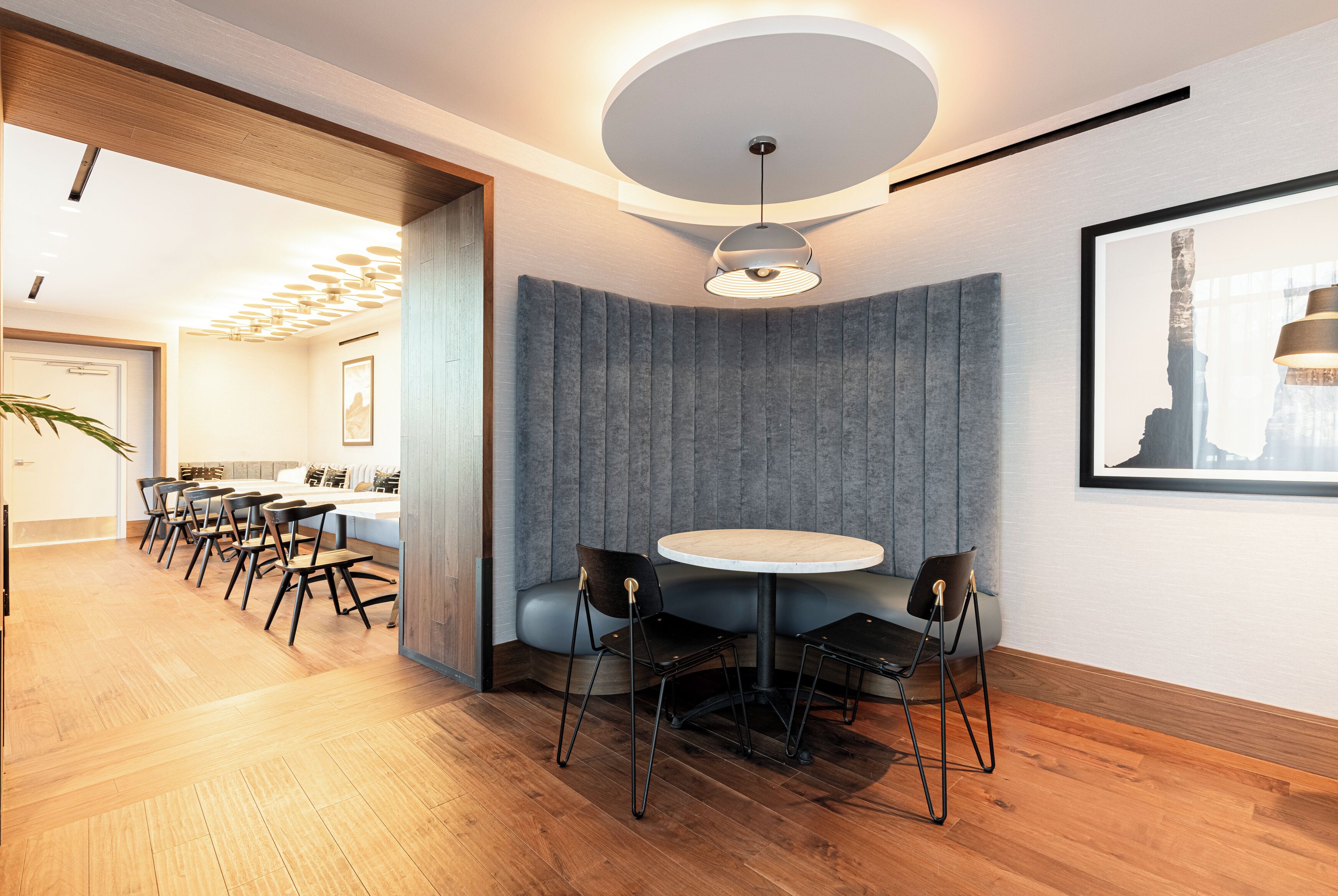 A modern interior with a round table, chairs, a ceiling light, and a framed picture on the wall.
