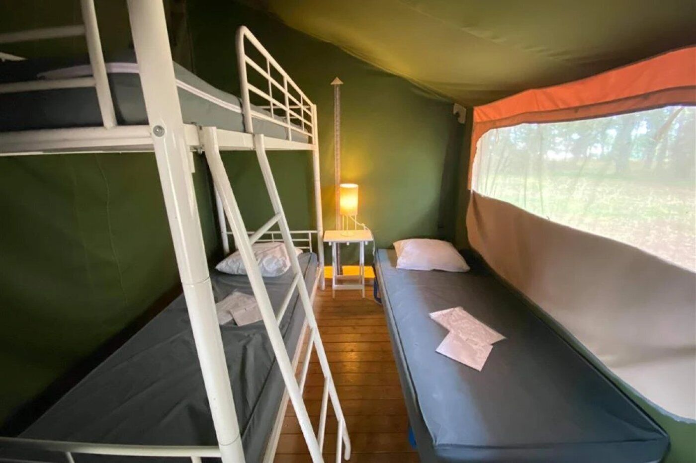 A bunk bed room with a table and lamp, green walls, and a window with a view.