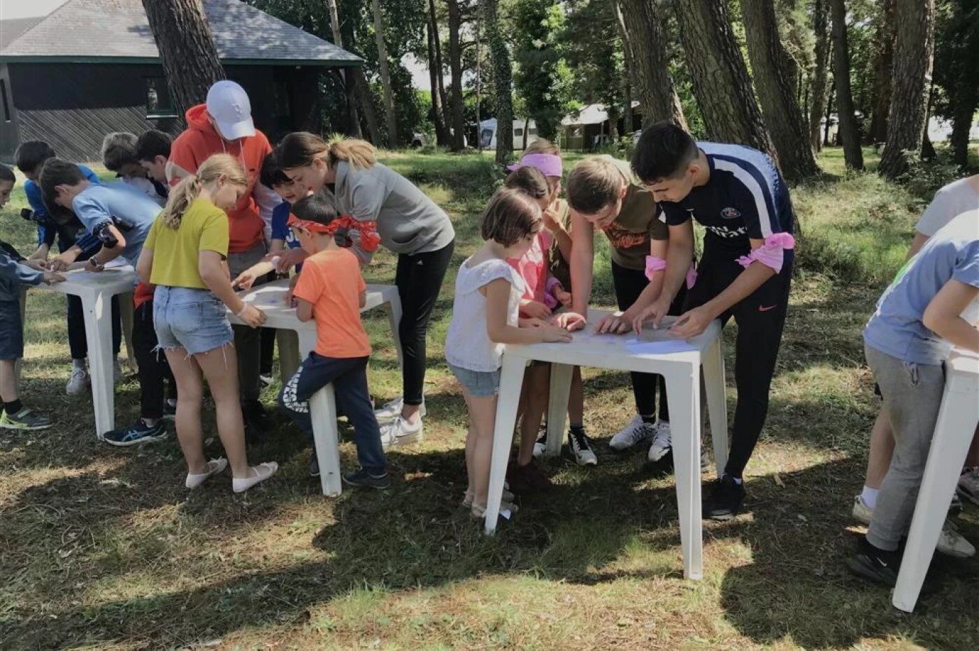 A group of children and adults gathered around tables outdoors, possibly engaged in an activity or game.