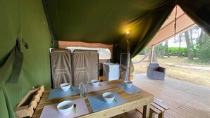 Een tentaccomodatie met een houten eettafel, een kleine koelkast en een hangmat buiten.