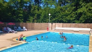 Une piscine avec des personnes à l’intérieur, entourée d’un mur de briques et d’arbres.