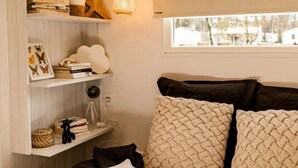 Une chambre à coucher comprenant un lit, une fenêtre, une étagère avec des livres et des objets décoratifs, et un luminaire suspendu.