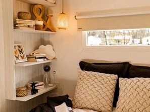 Ein Schlafzimmer mit Bett, Fenster, einer Regal mit Büchern und Dekoration sowie einer Pendelleuchte.