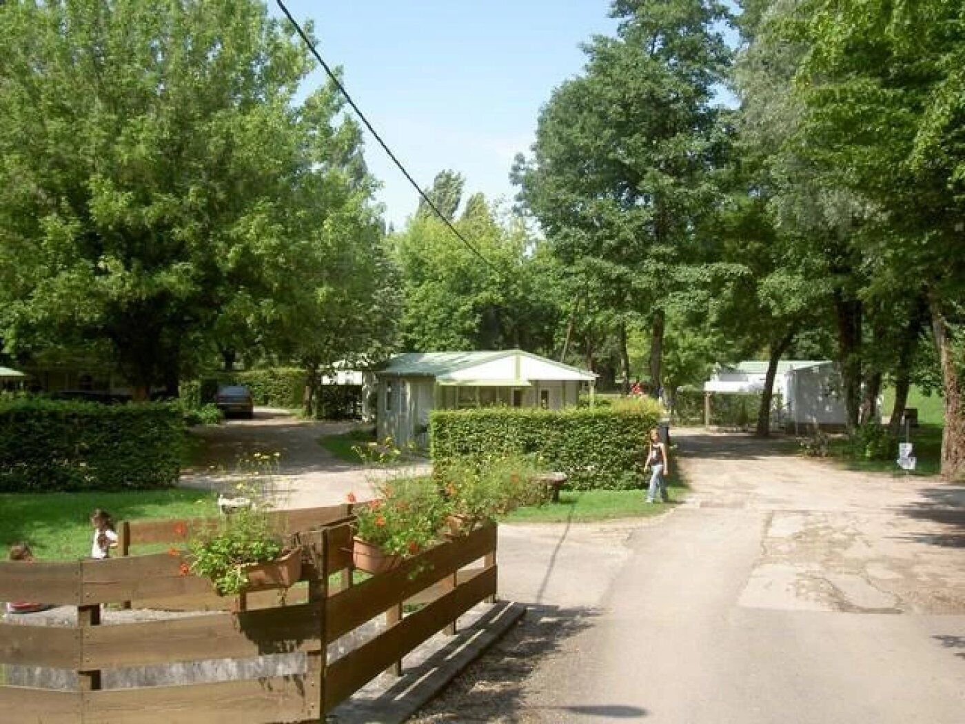Un camping con varias cabañas, una carretera pavimentada y una valla de madera con plantas en macetas.