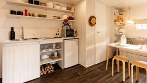 Une cuisine compacte avec des meubles blancs, un petit réfrigérateur et un coin repas comprenant une table et deux tabourets.