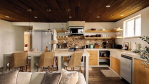 Una cocina moderna con protector de piedra, techo de madera y comedor con sillas de mimbre.