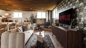 Una sala de estar con un sofá, una mesa de centro y un televisor de pantalla plana grande montado en la pared.