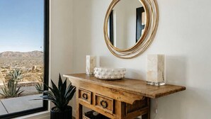 A wooden console table with a gold-framed mirror, two white candle holders, and a potted plant. - Solara Ridge • Serene Escape, Panoramic Views, Spa, and Cowboy Tub (Yucca Valley)