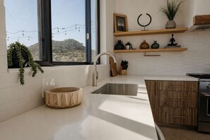 A modern kitchen with a large window, a wooden bowl sink, and a built-in stove. - Solara Ridge · Hilltop Views, Hot Tub, Cowboy Tub (Yucca Valley)