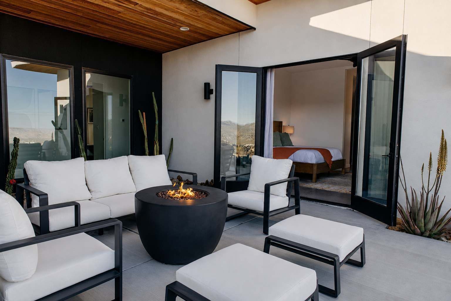 An outdoor seating area with a fire pit, white cushioned chairs, and a view of the interior.