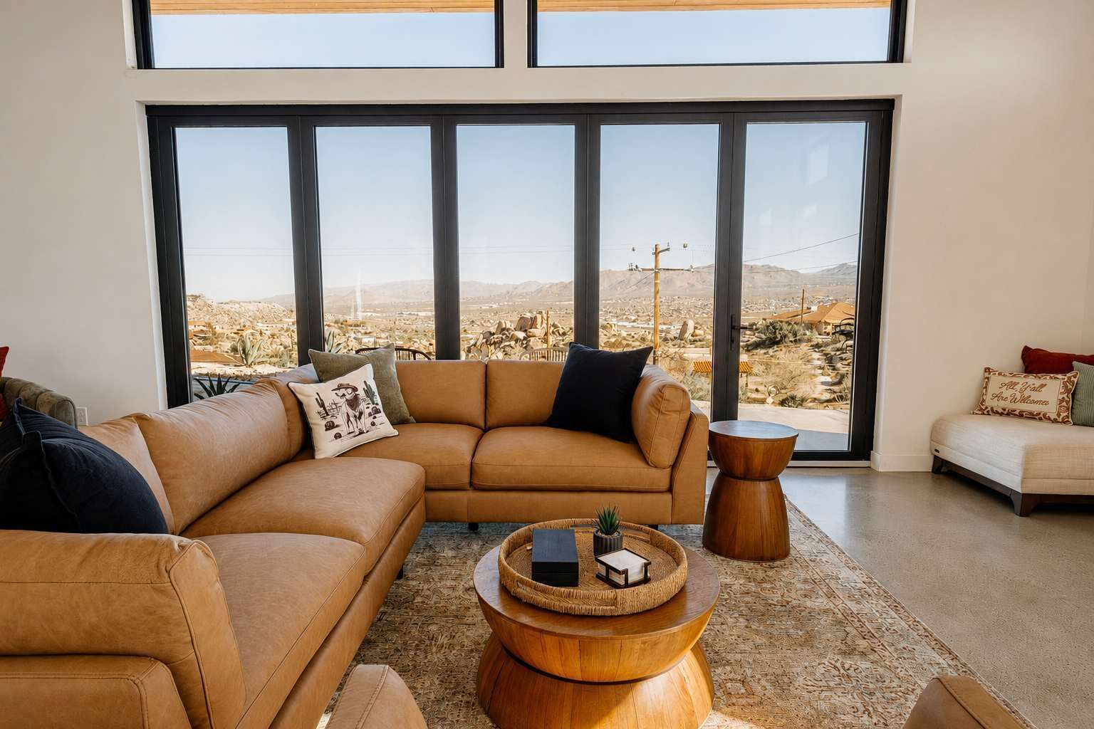 A modern living room with a large sectional sofa, a coffee table, and a view of a desert landscape through large windows.