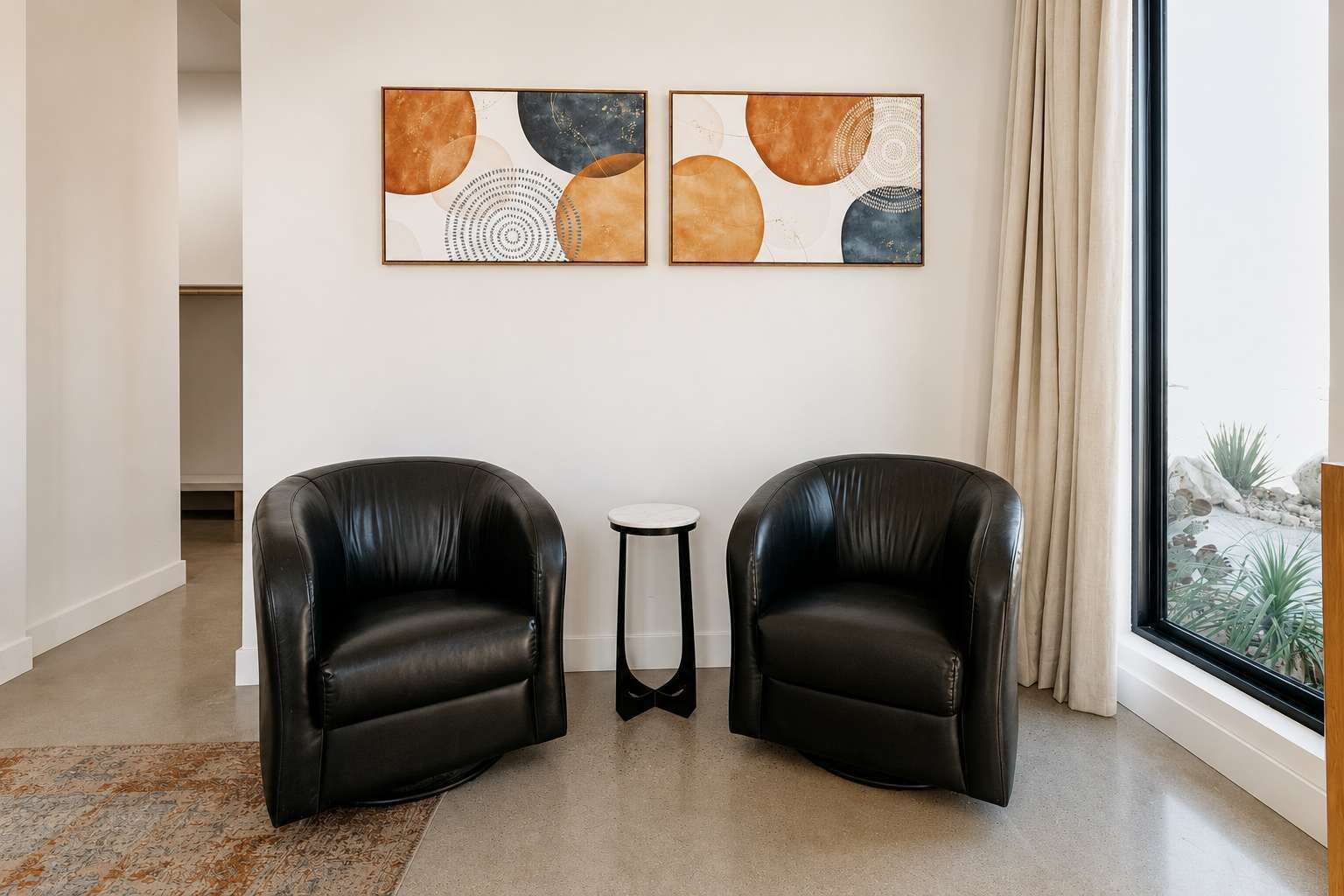 Um quarto com duas poltronas de couro preto, uma pequena mesa branca e duas pinturas abstratas na parede.