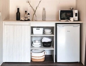 A compact kitchen with a microwave, a small refrigerator, and shelves with dishes and a basket. - ZEcamping 4* piscine club enfant  locatif 16m2 4 pers (Lons)