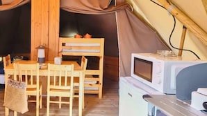 A tent interior with a wooden table, chairs, a small kitchenette, and a sleeping area. - ZEcamping 3 étoiles piscine chauffée tente 18m2 (Lussas)