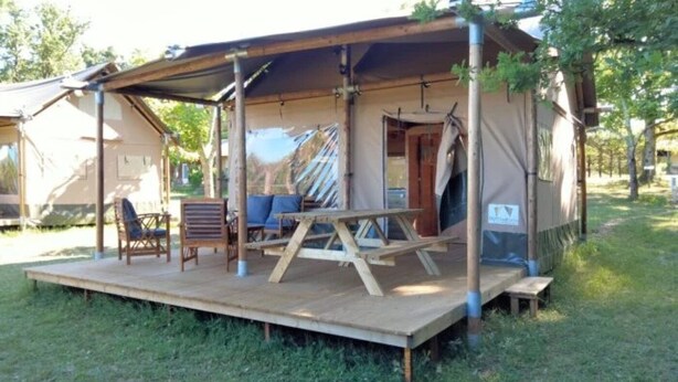 Un'area salotto all'aperto coperta, con tavolo e sedie, una struttura a tenda e terreno erboso.