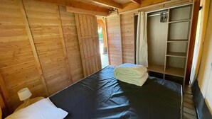 A wooden cabin room with a bed, a small table, and a wardrobe. - ZEcamping 3* piscine chiens acceptés locatif BBQ 72m2 5 pers (Dévillac)