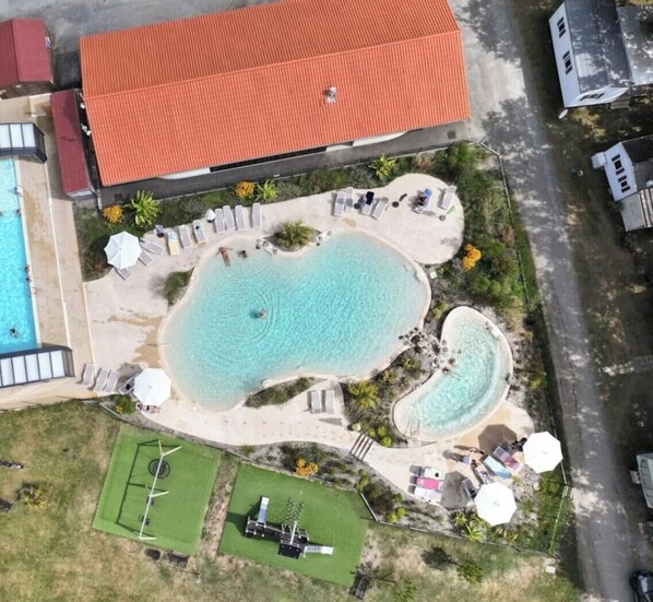 Luftaufnahme eines Resorts mit einem großen zentralen Pool, mehreren kleineren Pools und einem Tennisplatz.