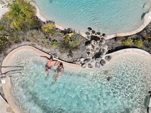 Vista aérea de una zona de piscina con agua cristalina, rodeada de rocas y vegetación tropical.