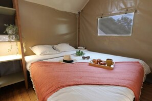 Una habitación tipo tienda de campaña con una cama, una ventana, un estante con plantas y una bandeja con comida.