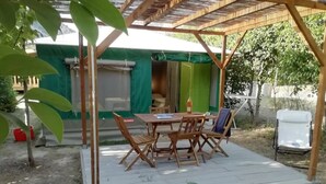 Een overdekt terras met een houten tafel en stoelen, een witte stoel en een kleine plant.