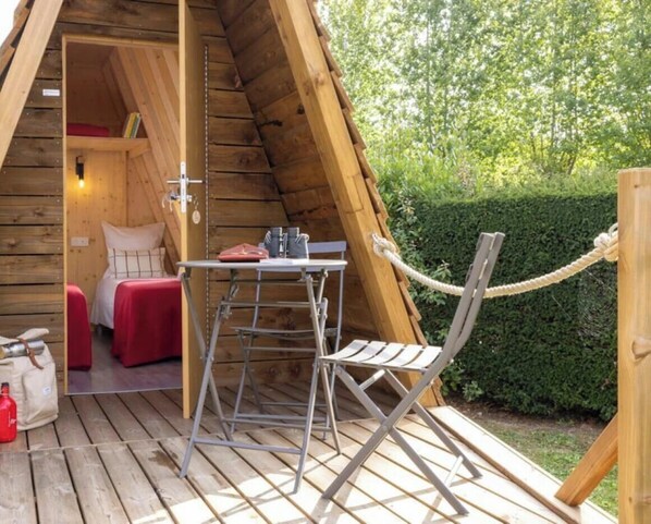 A wooden A-frame structure with a bed, a table, and a chair on the deck. - ZEcamping 4* 1km plage piscine chauffée fitness locatif 8m2 2 pers (Saint-Jean-de-Monts)