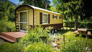 Uma casa móvel com varanda coberta, mesa para piquenique e um jardim.